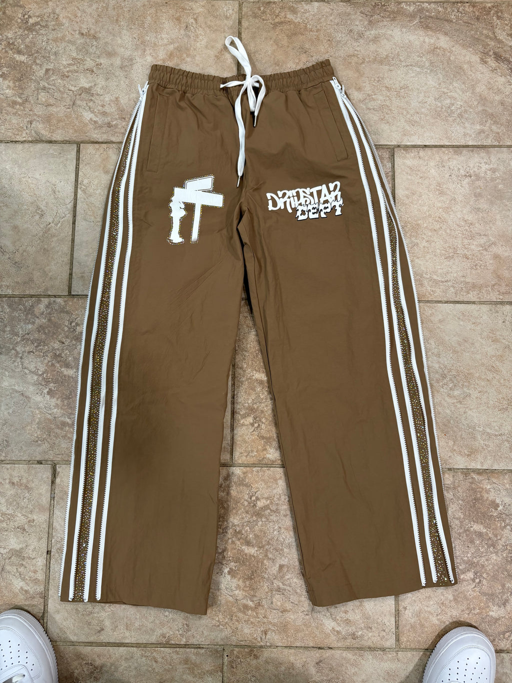 Brown track pants with white stripes on a tiled floor