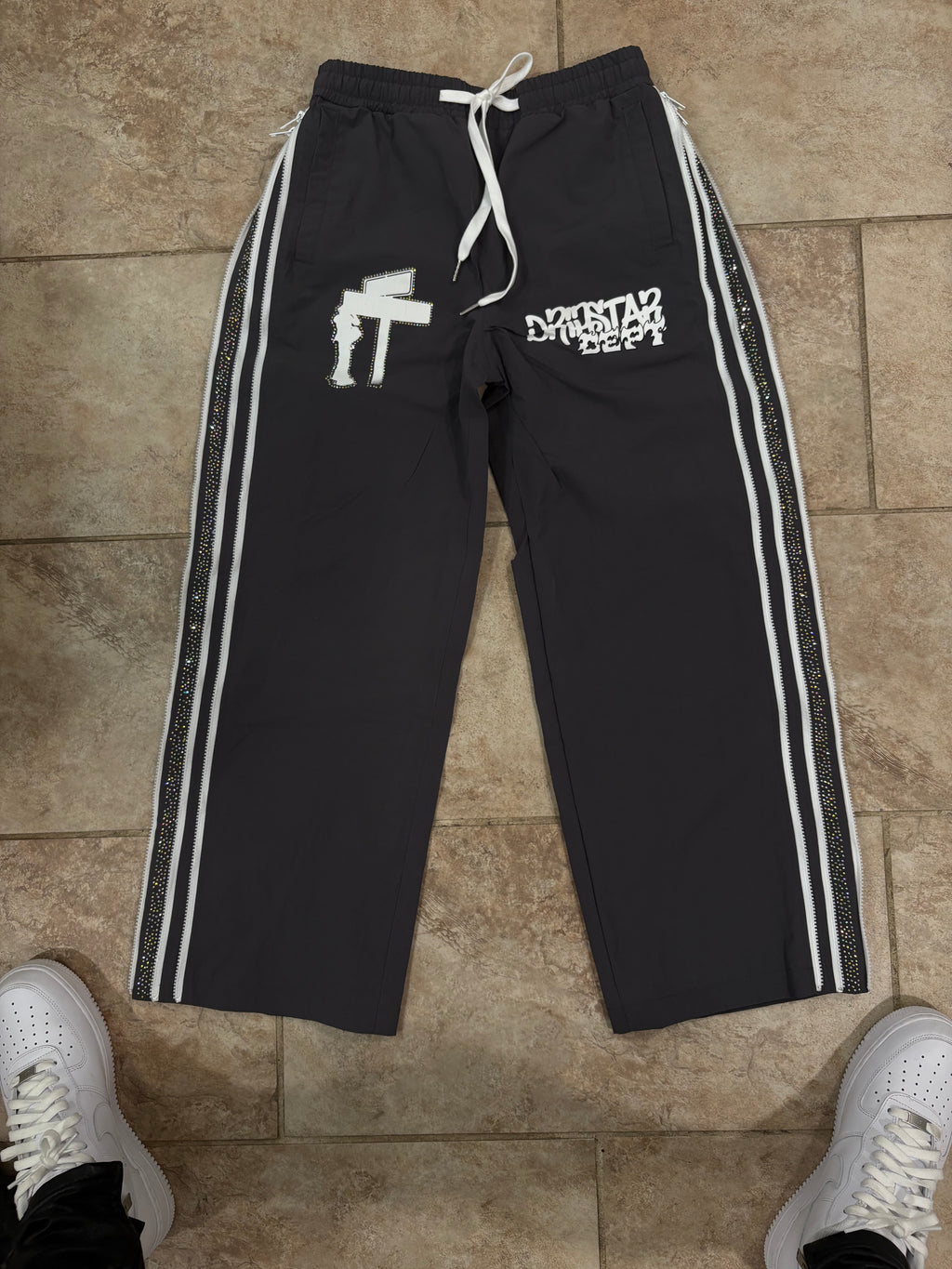 Gray track pants with white stripes and text on a tiled floor.
